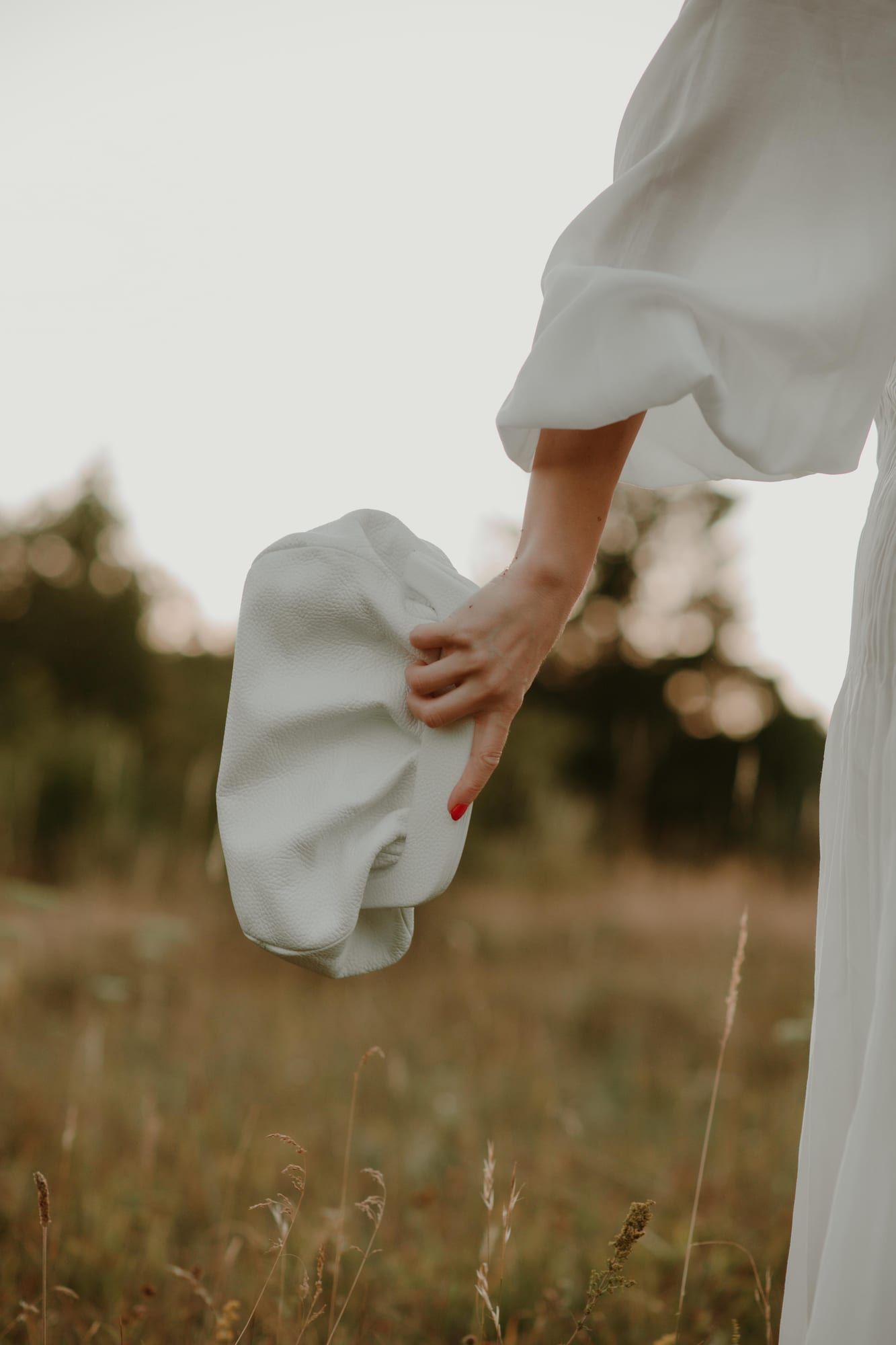 Bela PELEZZE pouch tašna nošena u polju uz belu haljinu